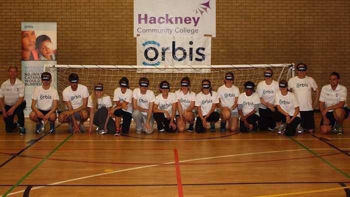 Blindfolded footballers and their coach kneel by a goal with the Orbis logo displayed
