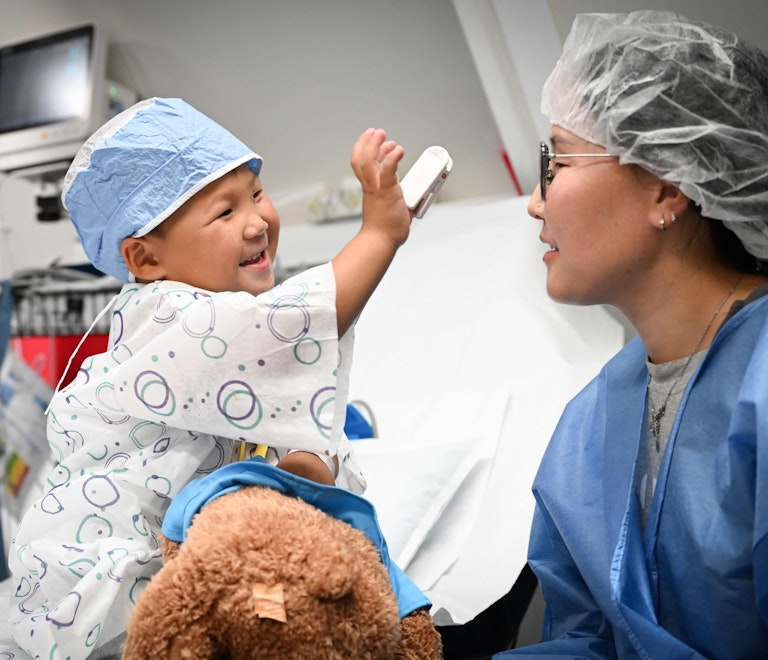 A young girl in scrubs smiles at a doctor before surgery.